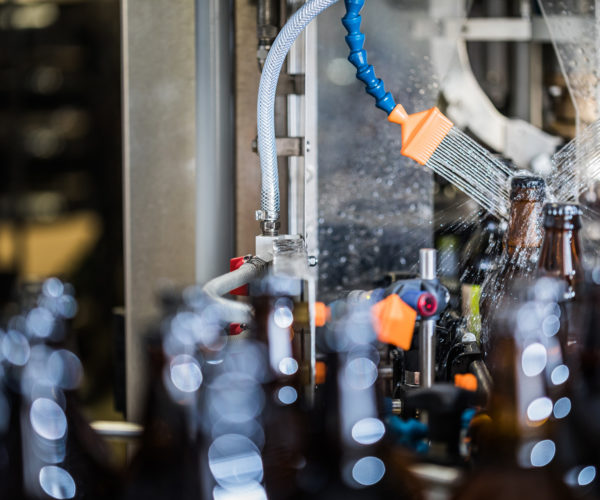 Brown glass bottles being washed with water after filling and bottling on conveyor.